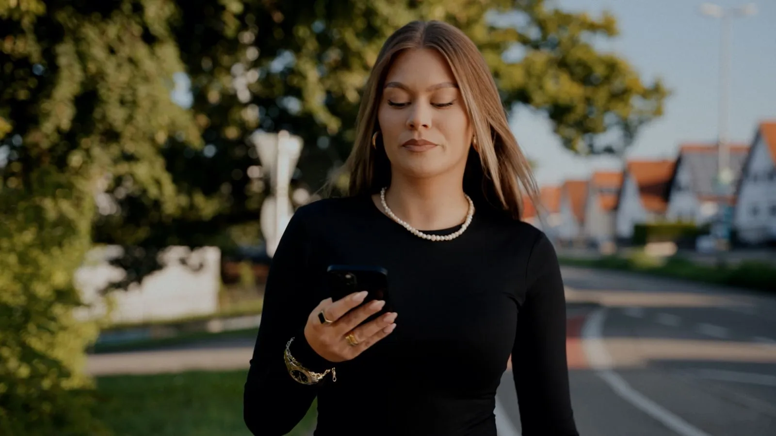 Eine Frau in schwarzem Oberteil schaut auf ihr Handy und geht draußen auf einer Straße. Foto/Video von Felix Weise, Medienproduktion für Sport, Outdoor & Events im Allgäu, Kempten und Bayern.