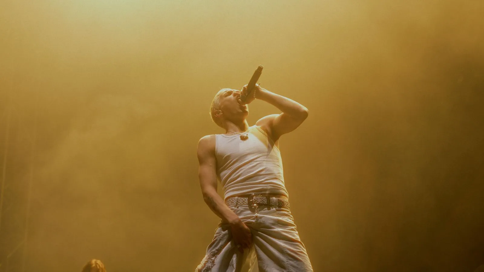 SOHO BANI mit weißem Tanktop und Hose singt leidenschaftlich ins Mikrofon auf der Bühne. Foto/Video von Felix Weise, Medienproduktion für Sport, Outdoor & Events im Allgäu, Kempten und Bayern.
