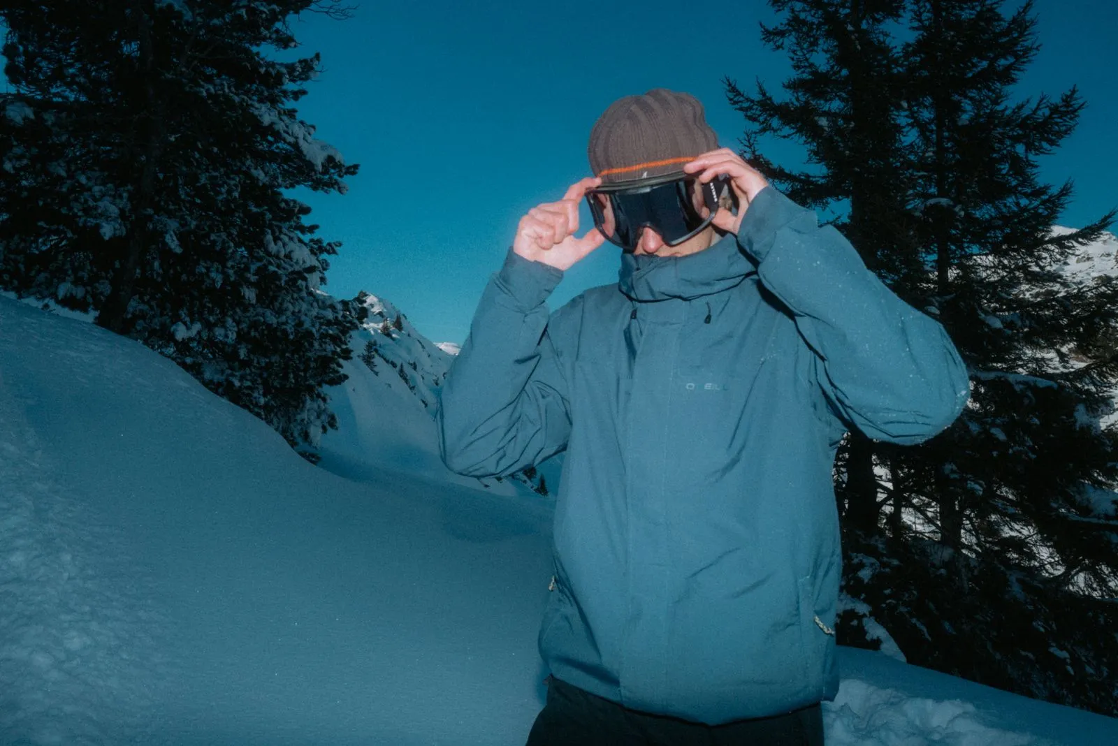 Person setzt im Schnee einer Berglandschaft eine Skibrille auf, trägt blaue Jacke und Mütze. Foto/Video von Felix Weise, Medienproduktion für Sport, Outdoor & Events im Allgäu, Kempten und Bayern.