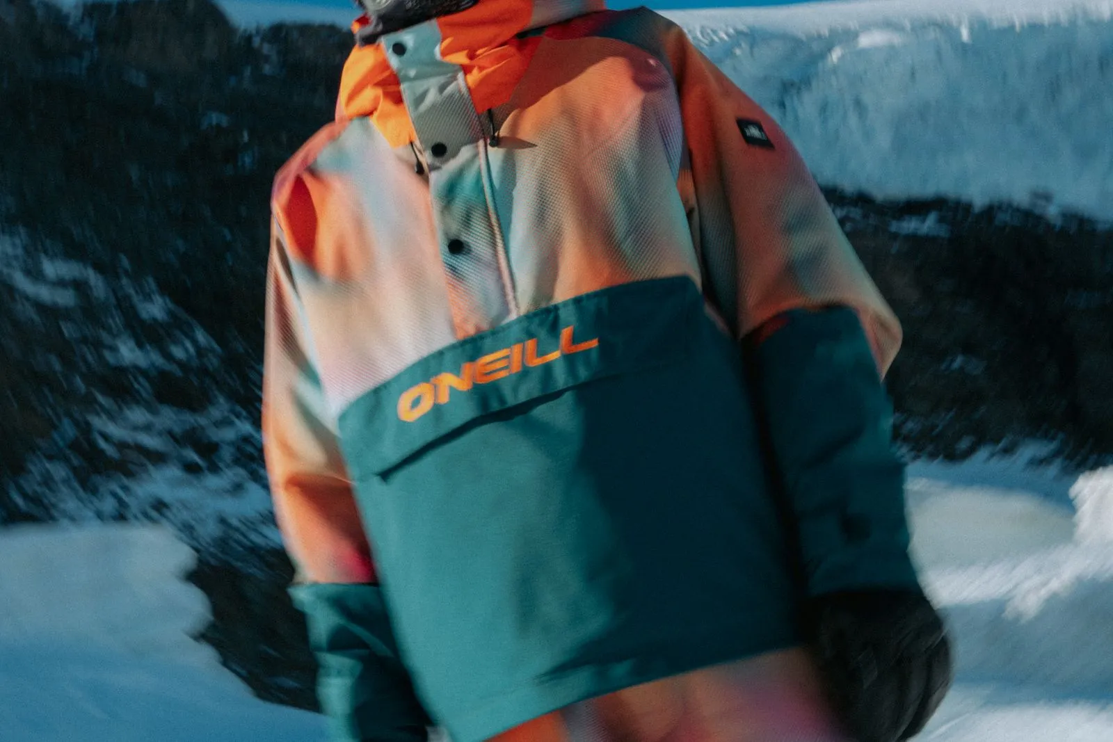 Person trägt bunte ONeill-Snowboardjacke vor schneebedecktem Berghintergrund. Foto/Video von Felix Weise, Medienproduktion für Sport, Outdoor & Events im Allgäu, Kempten und Bayern.