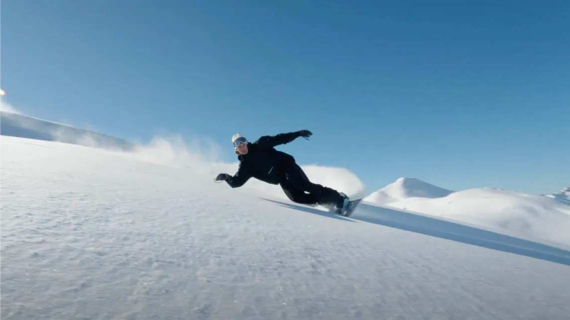Eine Person in schwarzer Winterkleidung fährt auf einer schneebedeckten Piste mit einem Snowboard bei klarem Himmel. Foto/Video von Felix Weise, Medienproduktion für Sport, Outdoor & Events im Allgäu, Kempten und Bayern.