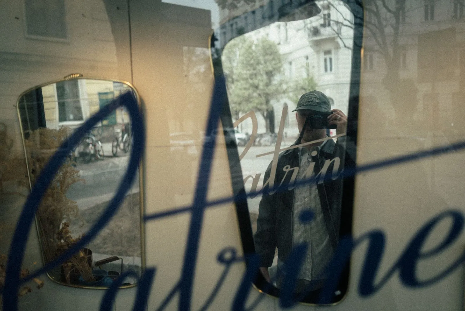 Person mit Basecap macht Foto durch eine Glasscheibe mit blauer Schrift und reflektiert Stadtleben. Foto/Video von Felix Weise, Medienproduktion für Sport, Outdoor & Events im Allgäu, Kempten und Bayern.