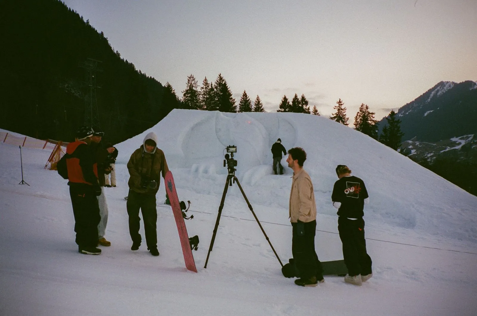 Gruppe von Menschen mit Snowboards vor einer großen verschneiten Skulptur in den Bergen bei Dämmerung. Foto/Video von Felix Weise, Medienproduktion für Sport, Outdoor & Events im Allgäu, Kempten und Bayern.