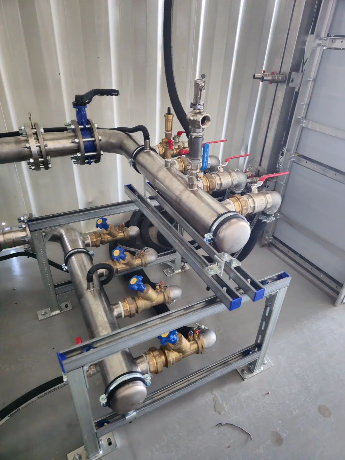 Industrial metal piping system with valves, supported by a metal frame inside a facility.