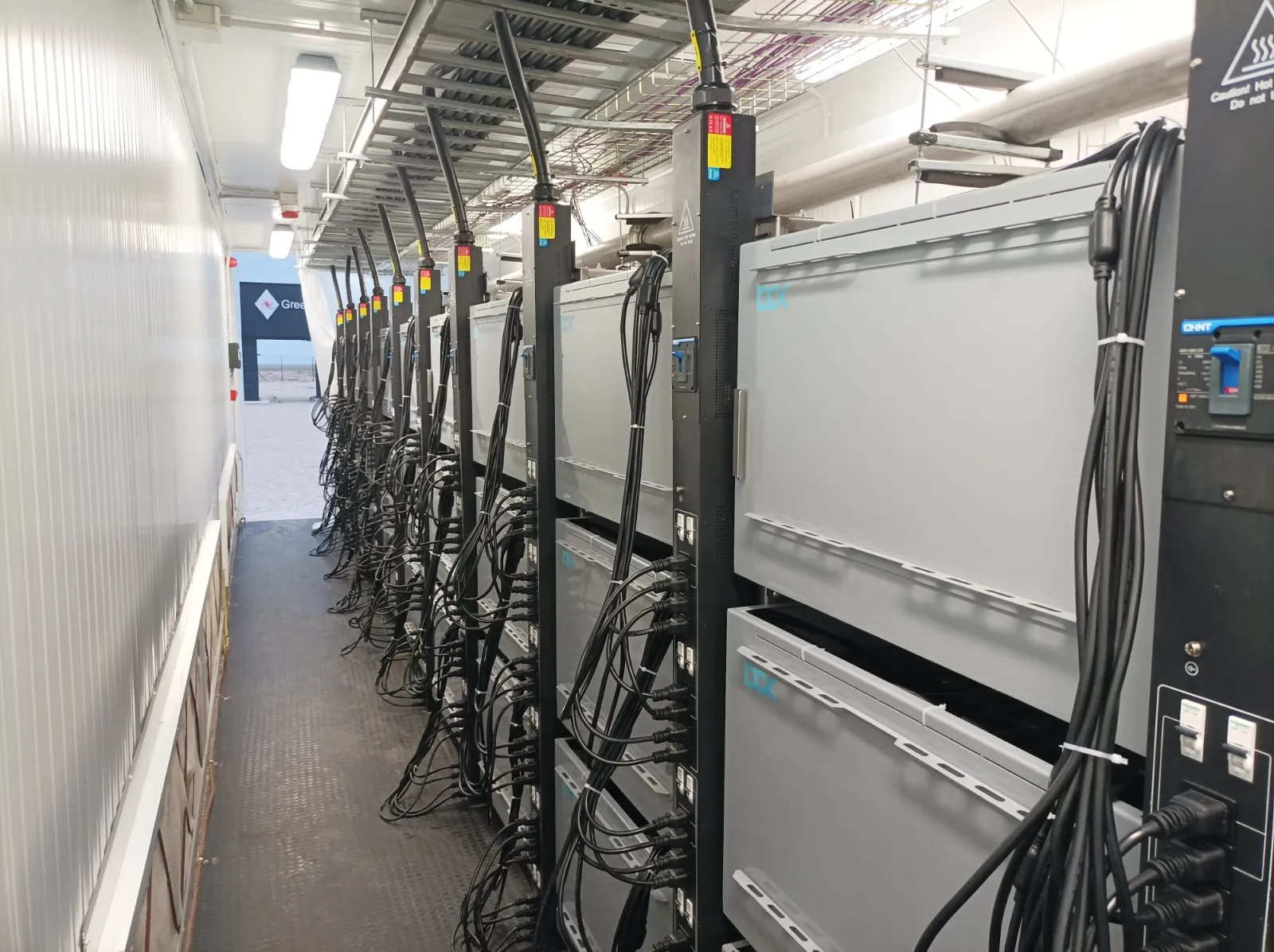 Interior view of a narrow corridor housing large electrical cabinets with numerous black cables.