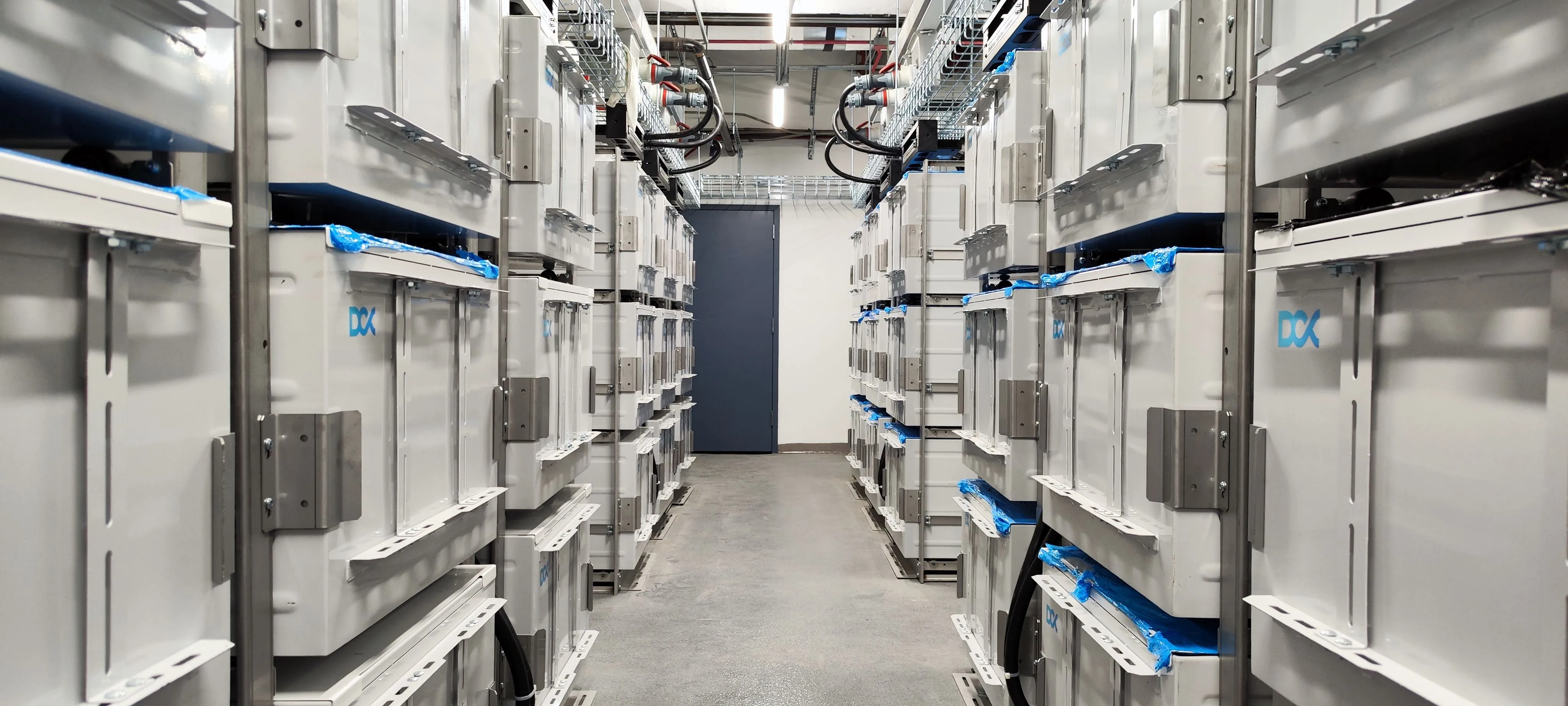 Corridor between rows of large industrial battery storage units with a closed door at the end.