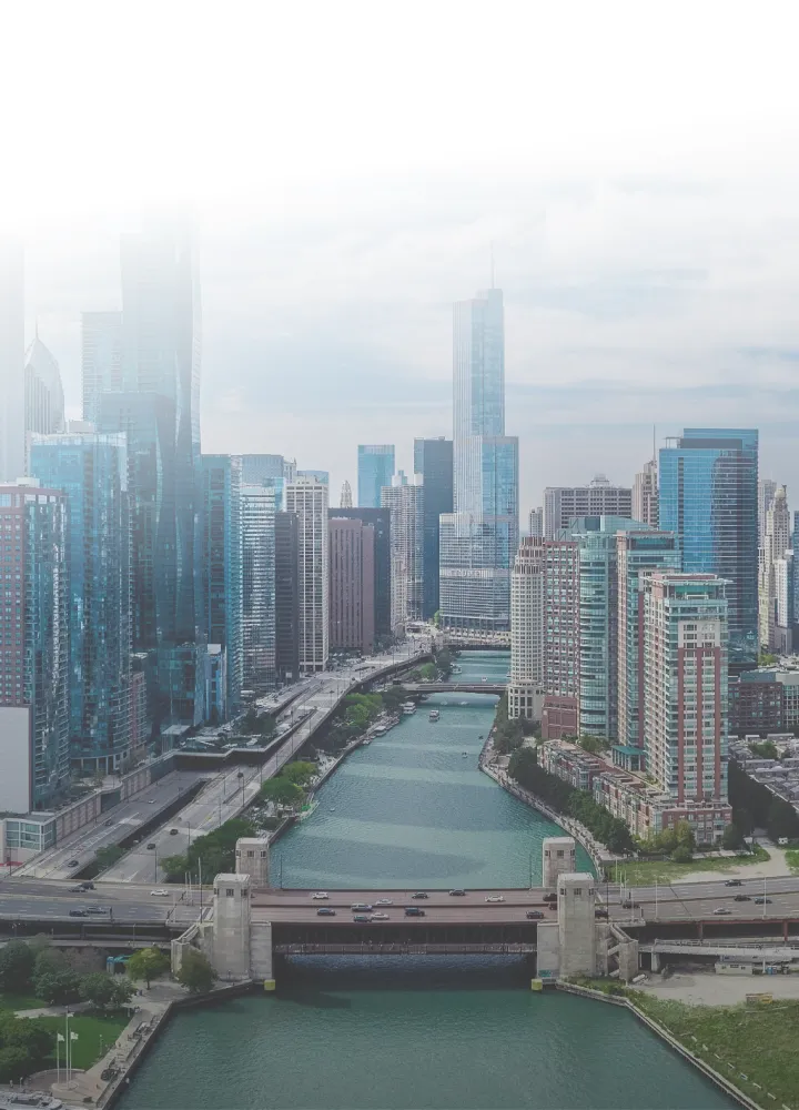 View of a river flowing through a city with tall skyscrapers on both sides and a bridge crossing it.