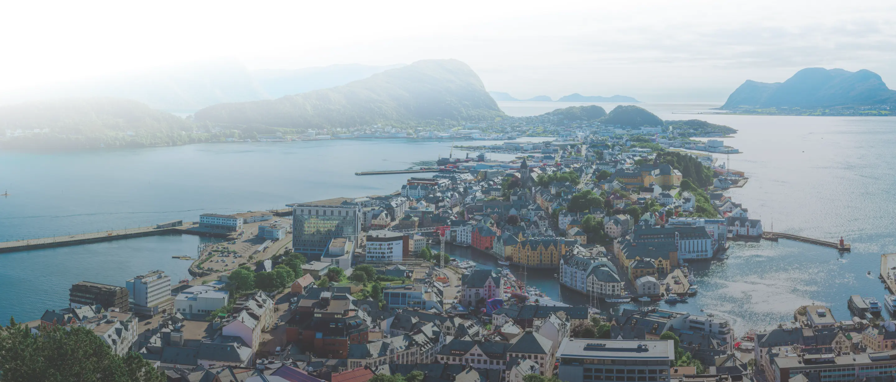 A coastal town with clustered buildings and boats surrounded by water and misty mountains in the background.