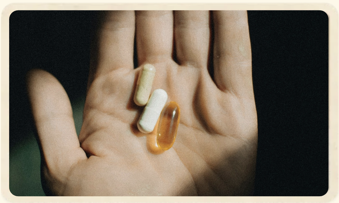 Flacons et gélules posés à côté d’un verre d’eau, d’une cuillère et d’un petit flacon transparent sur fond clair