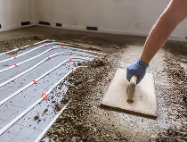 Person glättet Estrichboden mit einer Kelle in einem Raum, Fußbodenheizung sichtbar.