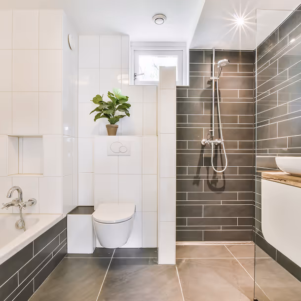 Modernes Badezimmer mit grauen und weißen Fliesen, freihängendem WC, Dusche mit Glasabtrennung und einer Topfpflanze auf einer Ablage.