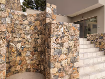 Treppenaufgang neben einer Mauer aus unregelmäßigen Natursteinen unter einem modernen Gebäude.