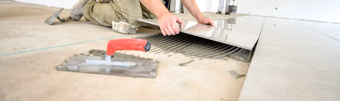Handwerker verlegt Fliesen auf Boden mit Kelle und Fliesenkleber.