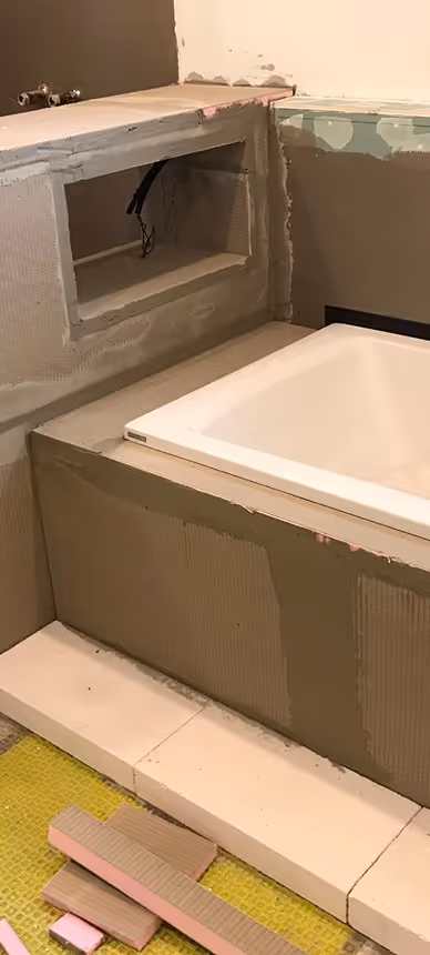 Teilweise fertiggestelltes Badezimmer mit eingebauter Badewanne und einer Futteröffnung an der Wand.