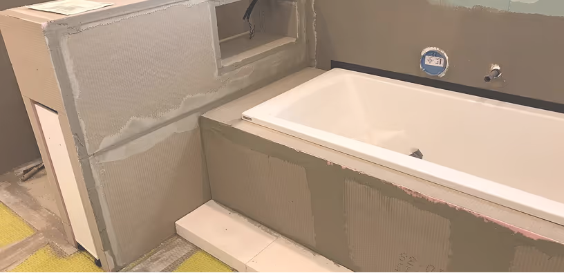 Unfertige Badewanne in einem Bad mit grauen Wänden, umgeben von teilweise verputzten Trockenbauwänden.