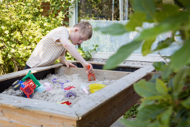 kind speelt in zandbak bij molenhuis