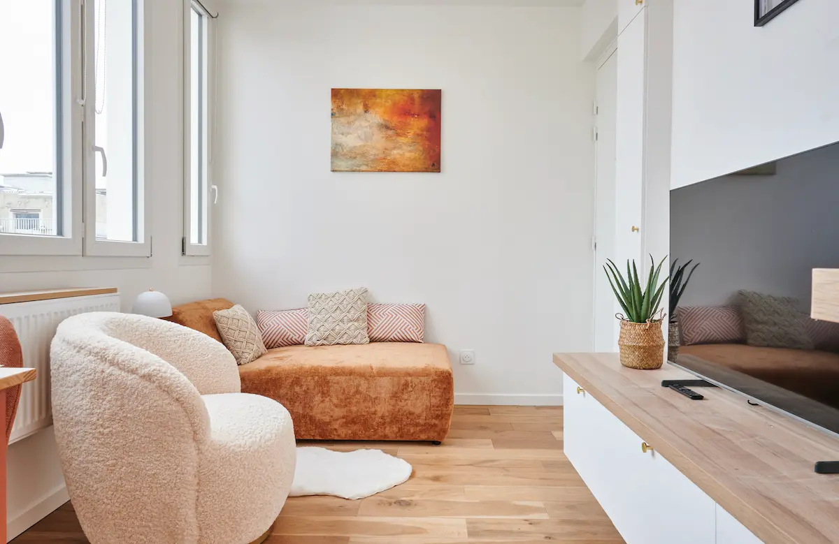 Salon clair et moderne aménagé par Mobimmo, avec canapé beige, coussins décoratifs et tableau abstrait, illustrant un ameublement locatif élégant et professionnel pour investisseurs Airbnb.