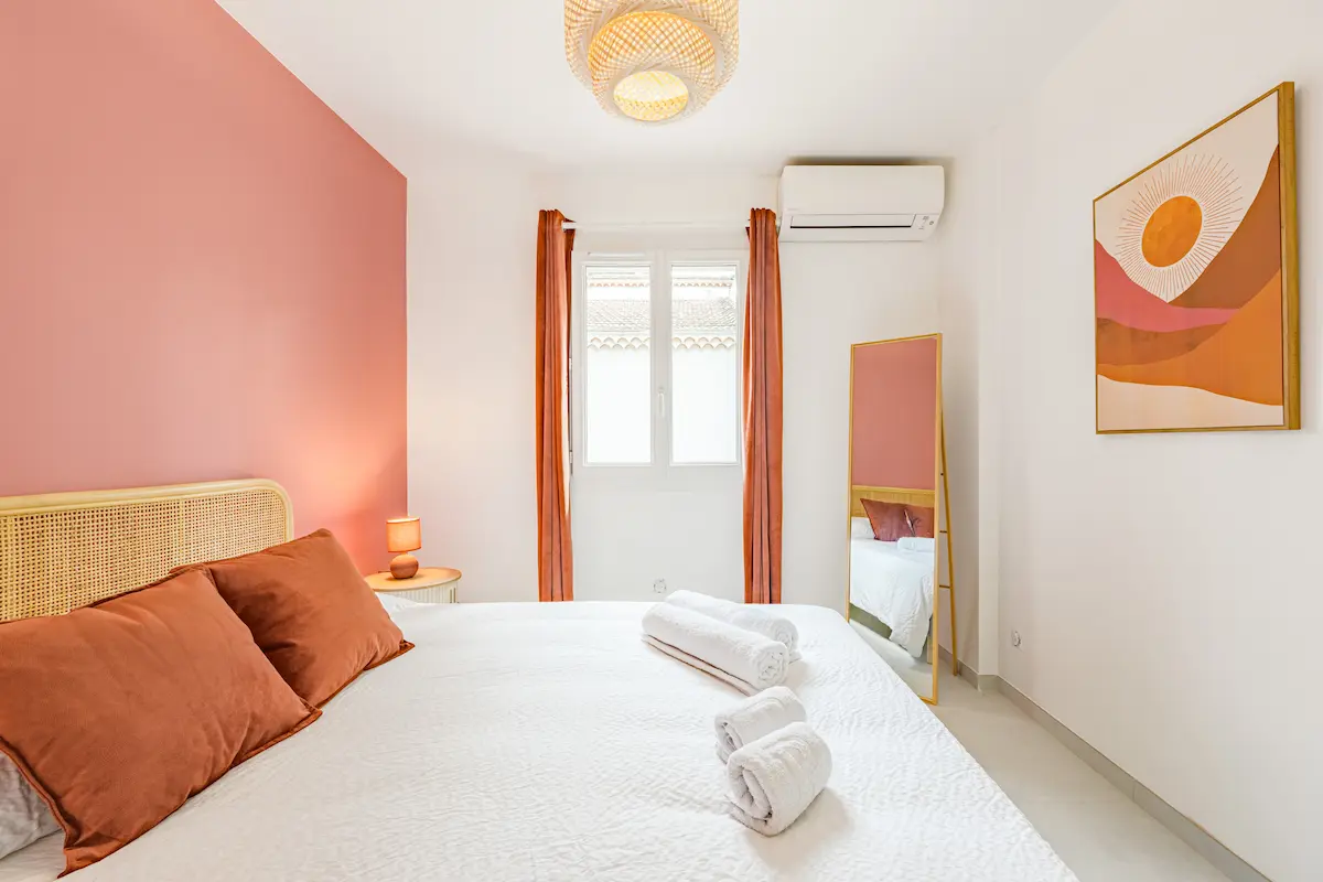 Chambre élégante meublée par Mobimmo, avec tête de lit en rotin, mur terracotta et tableau artistique, illustrant un ameublement inspiré par l’art conçu pour séduire les voyageurs Airbnb.