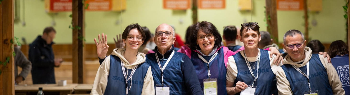 Un groupe de bénévoles souriants portant des gilets Salomon et des badges EcoTrail Paris, rassemblés dans une ambiance chaleureuse en intérieur, illustrant la convivialité et l’engagement des équipes.