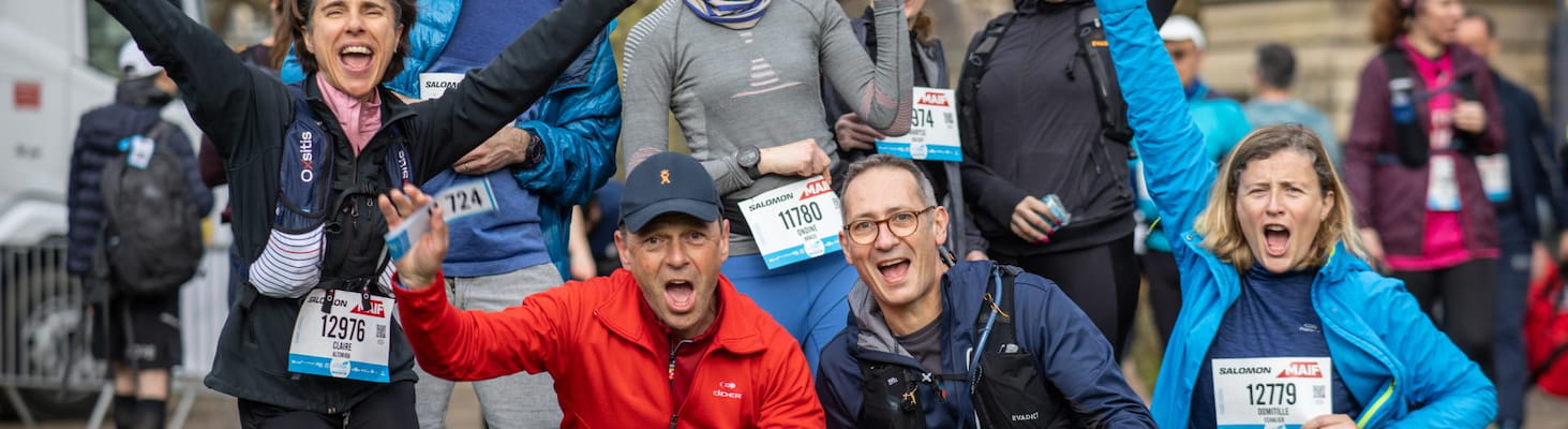 Un groupe de coureurs d'entreprise enthousiastes en tenue de course, levant les bras et souriant juste avant ou après l’effort, arborant leurs dossards EcoTrail Paris.