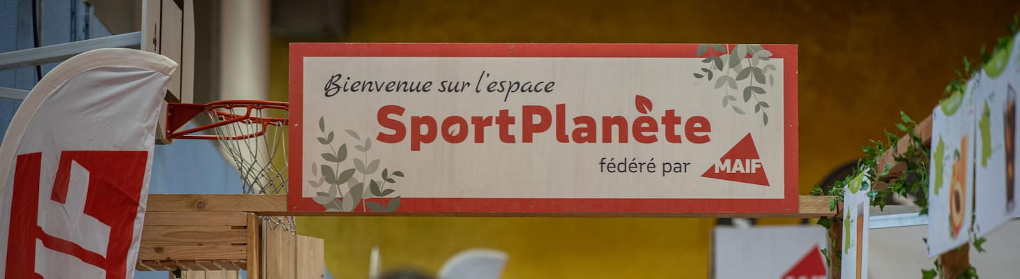 Pancarte "Bienvenue sur l’espace Sport Planète fédéré par MAIF" suspendue au-dessus d’un stand décoré de feuillage dans le village EcoTrail.