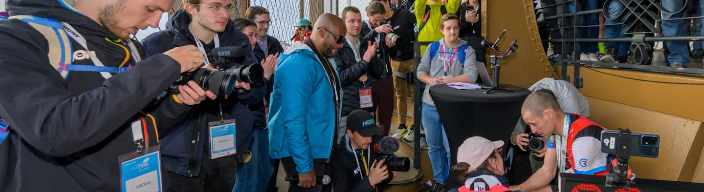 Photographes et journalistes capturant l’arrivée d’un coureur à l’EcoTrail Paris au sommet de la tour Eiffel, ambiance presse dynamique.