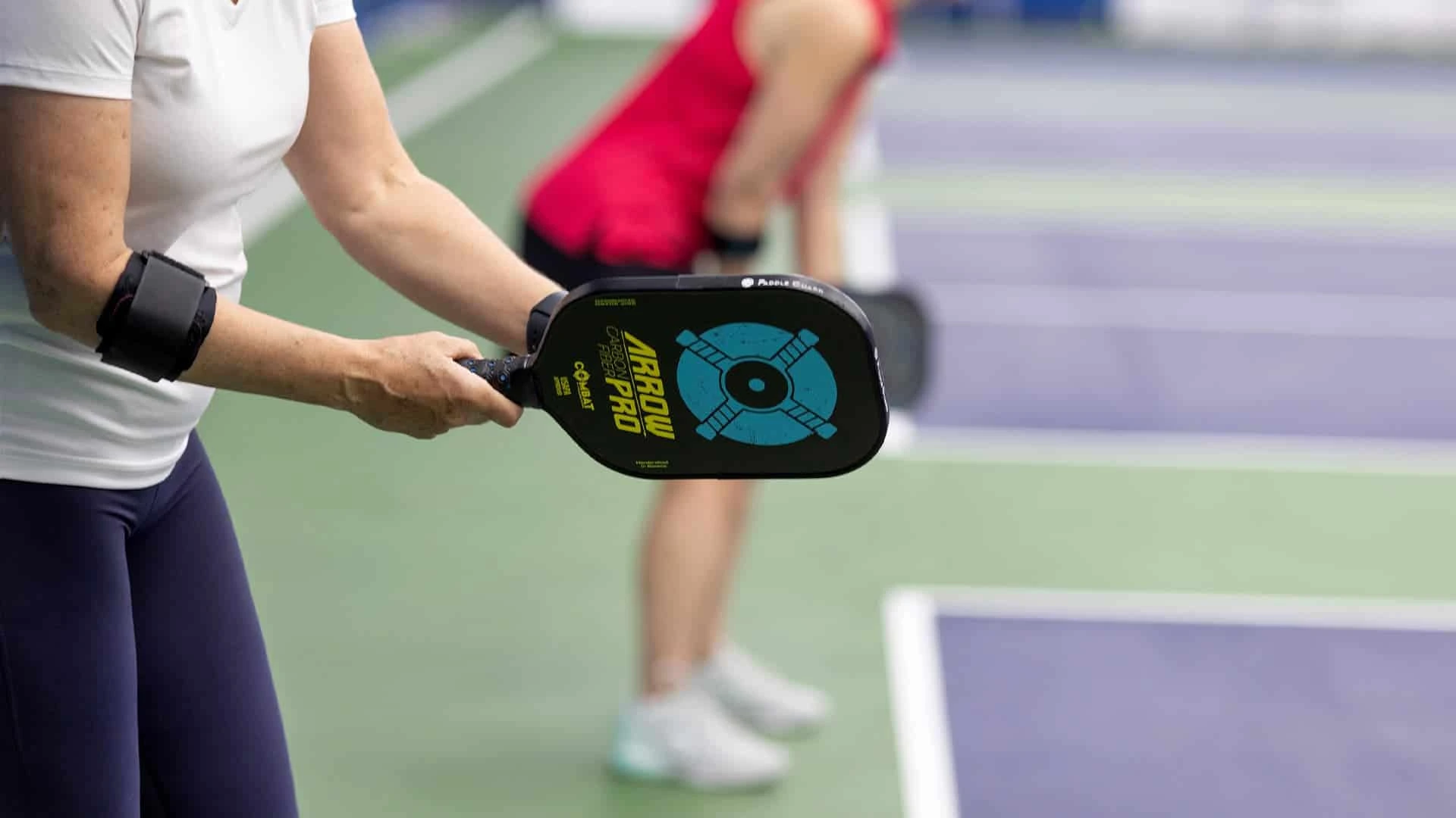Pickleball player wearing an elbow brace holding a branded paddle on the court