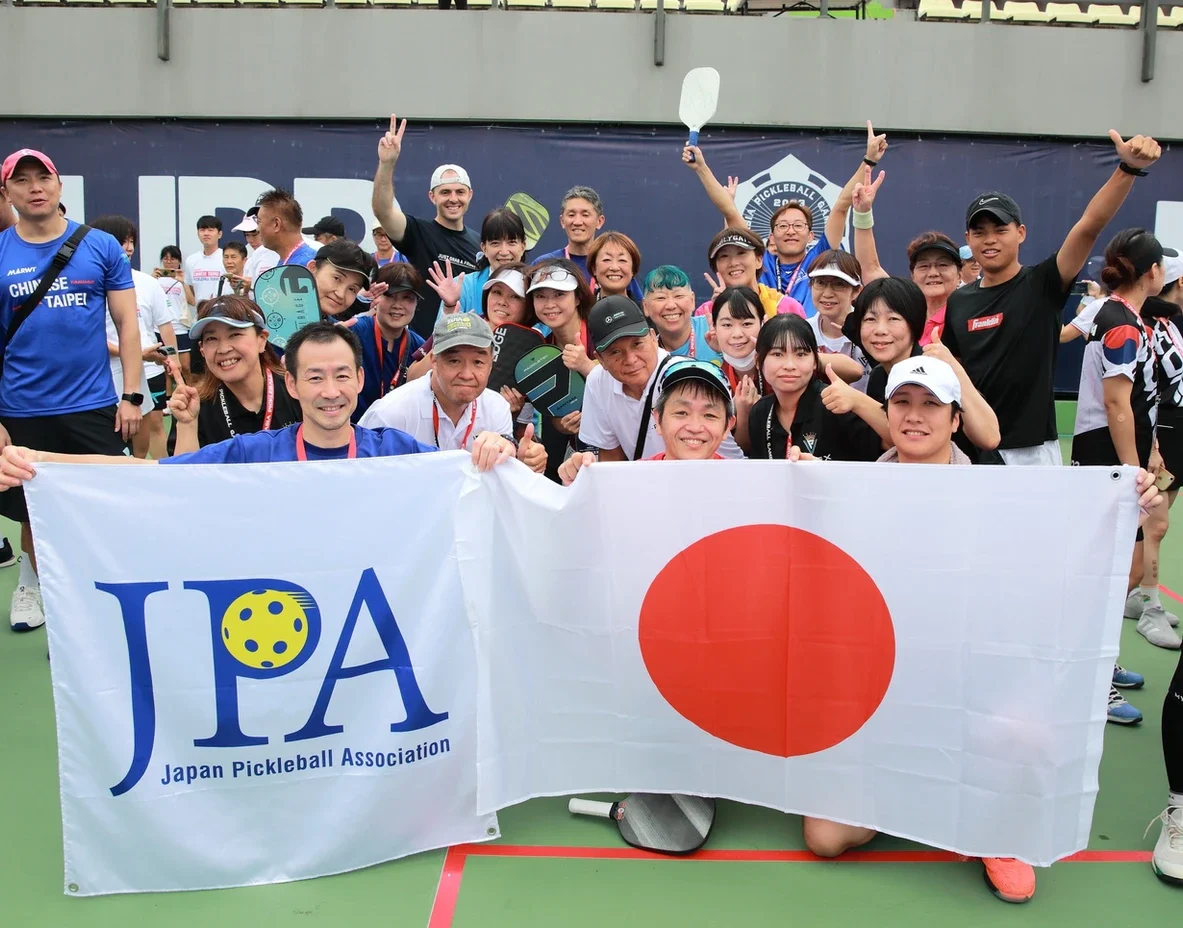 Japan Pickleball Association team celebrating at a tournament with their flag