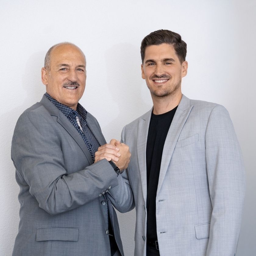 Yves und Urs Pfeuti von YU Broker AG in Worb in grauen Sakkos stehen nebeneinander vor weißem Hintergrund und geben sich mit beiden Händen einen freundschaftlichen Händedruck