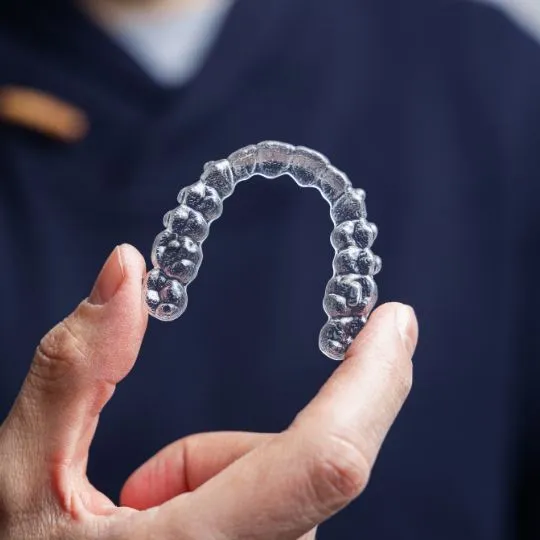 Close-up of hand holding a transparent clear aligner for orthodontic teeth straightening