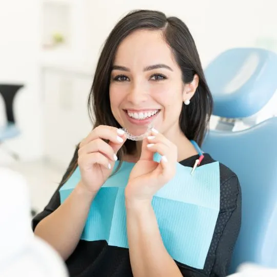 Happy dental patient holding clear aligners while sitting in chair at orthodontic clinic
