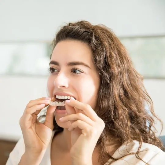 Young woman placing clear aligner trays on her teeth for orthodontic treatment at home