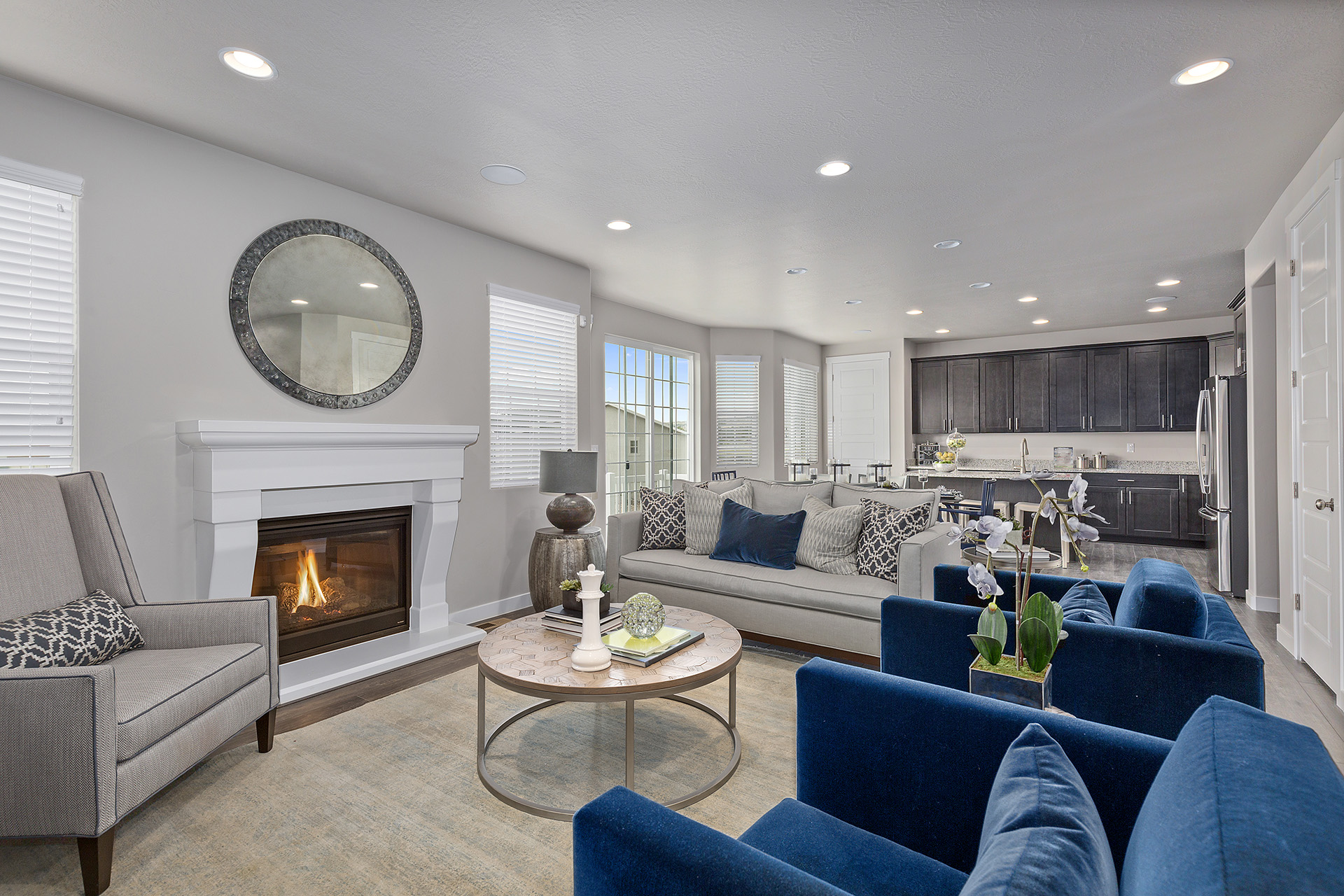 Living room with a fireplace, gray sofa, blue chairs, and a round coffee table with decor.