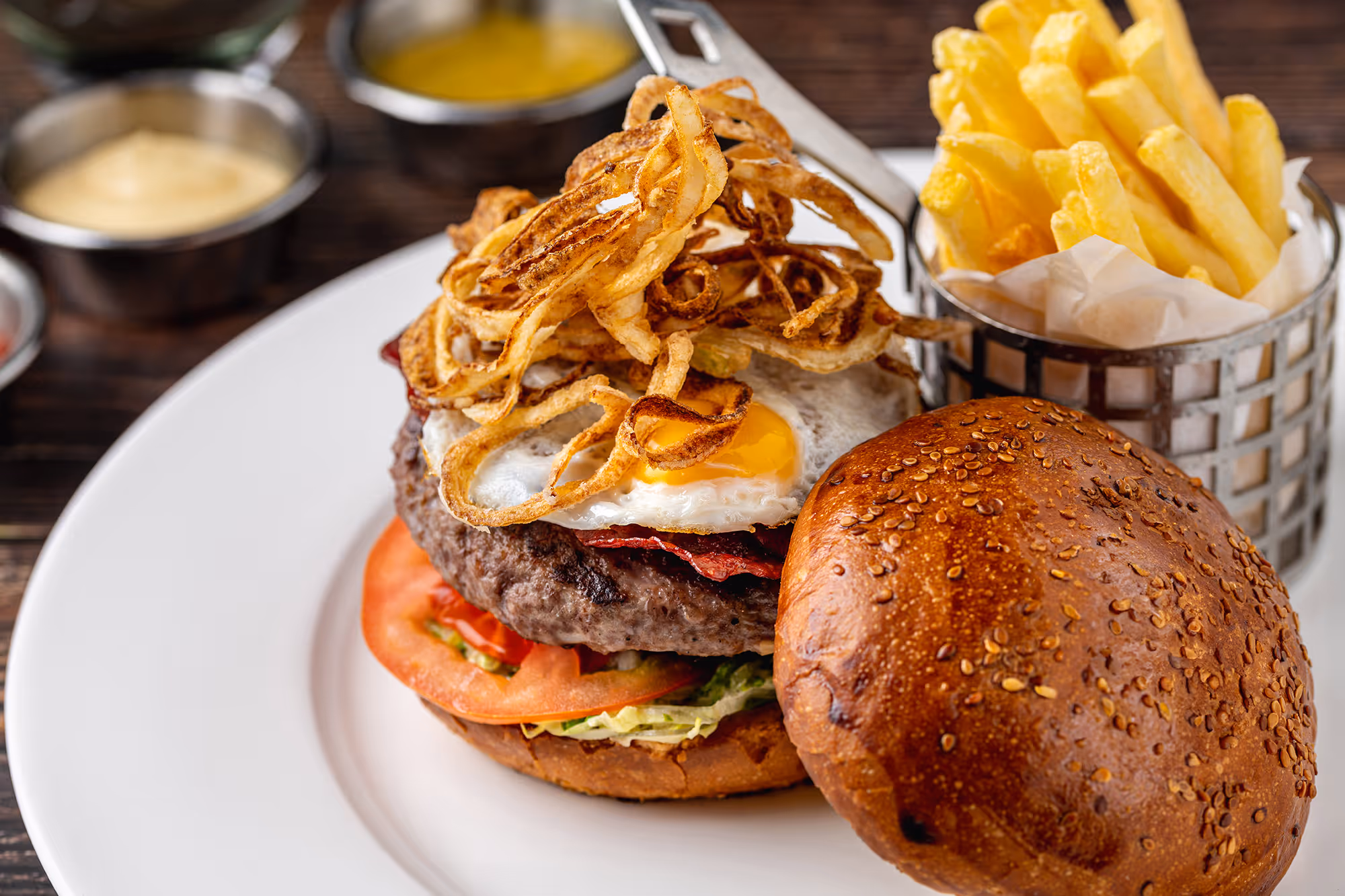 A burger with a fried egg and crispy onions, served with fries on a white plate.