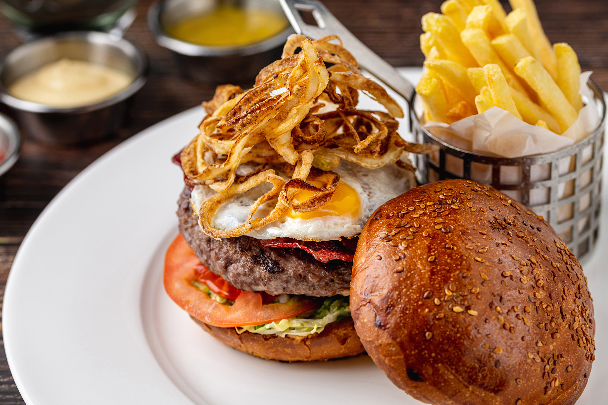 A burger with a fried egg and crispy onions, served with fries on a white plate.