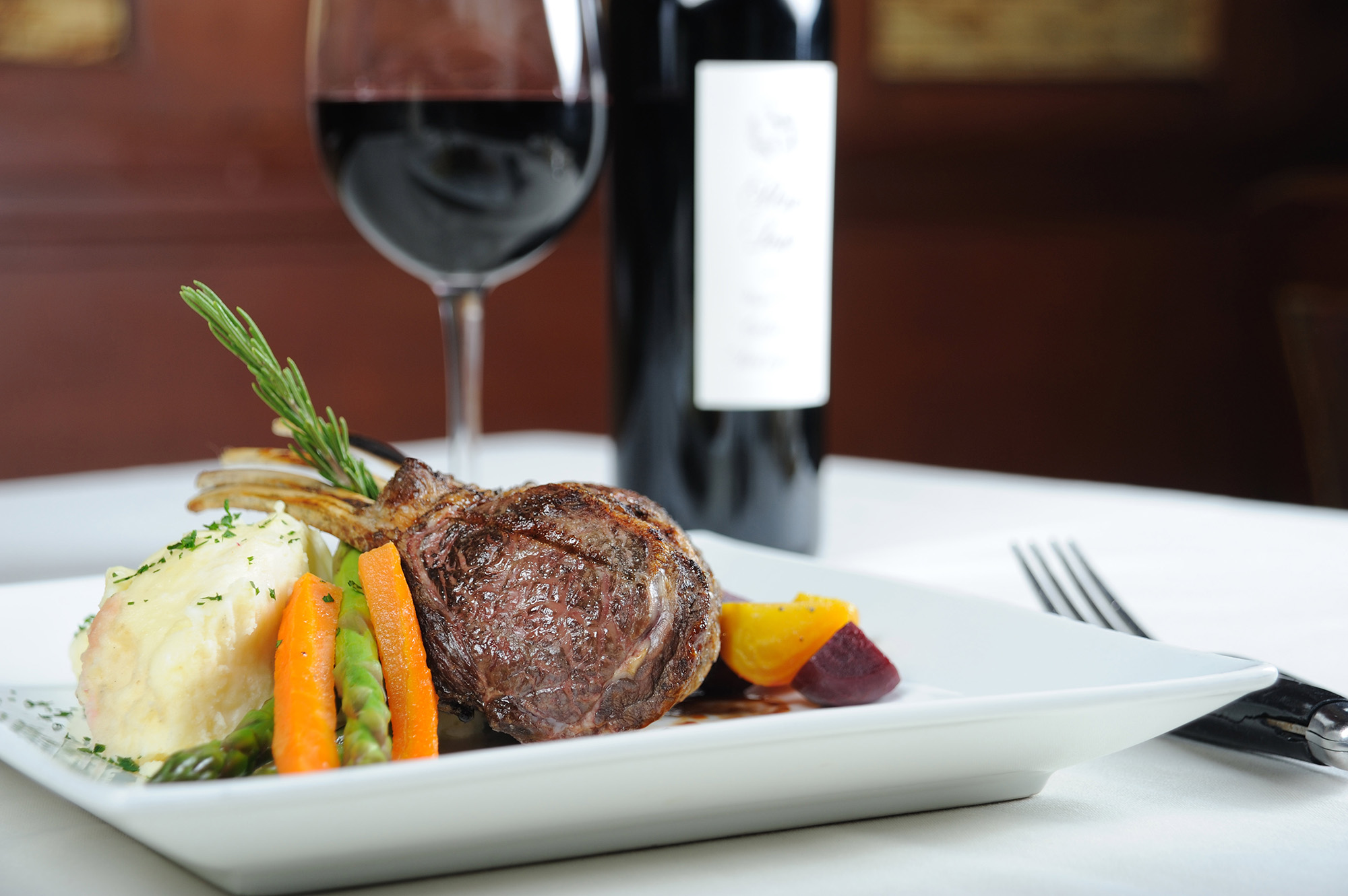A plate with steak, mashed potatoes, and vegetables next to a glass of red wine.