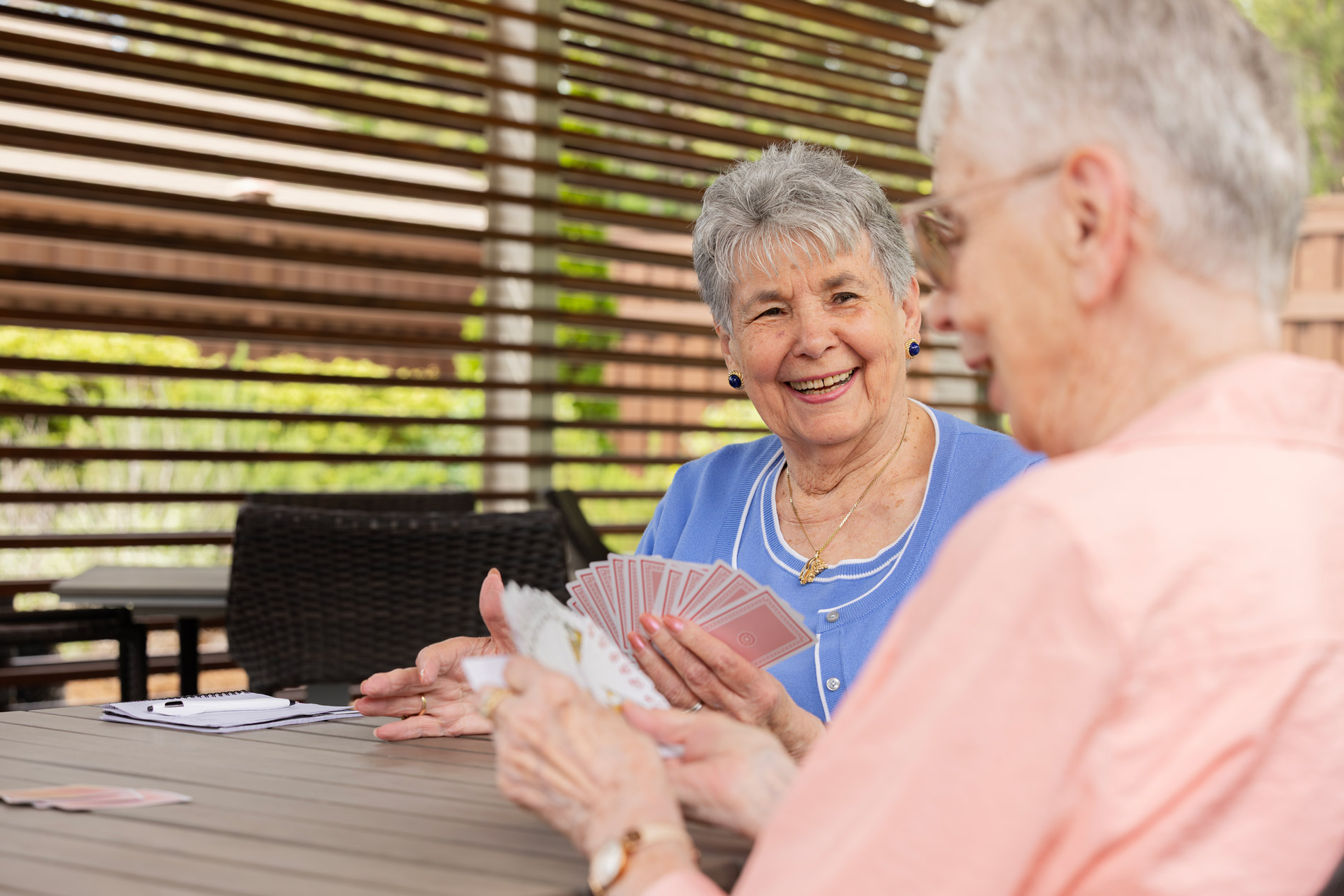 Two elderly women are sitting at a table playing cards, smiling and enjoying the game.
