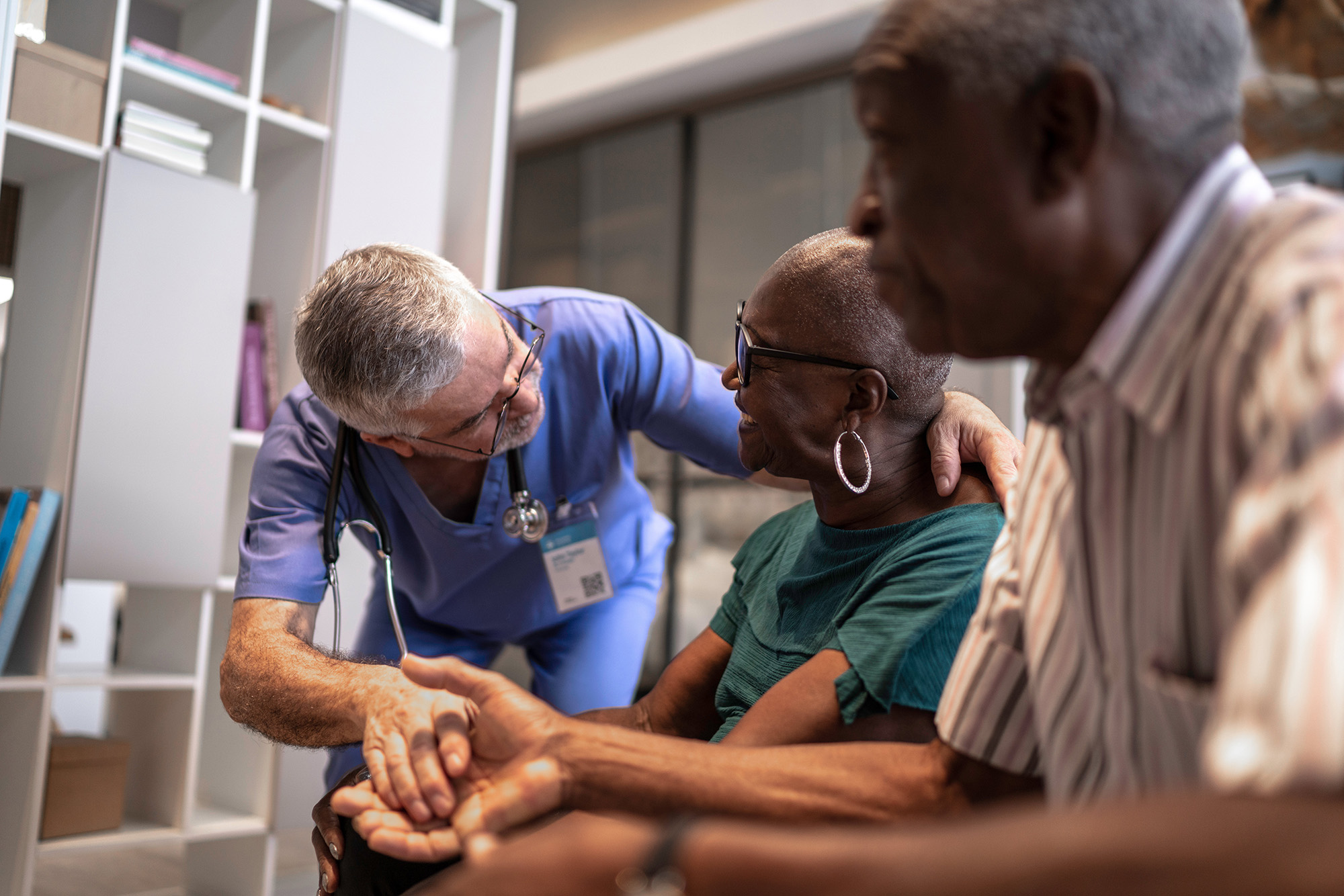 A healthcare professional comforts an elderly woman, holding her hand and smiling at her.