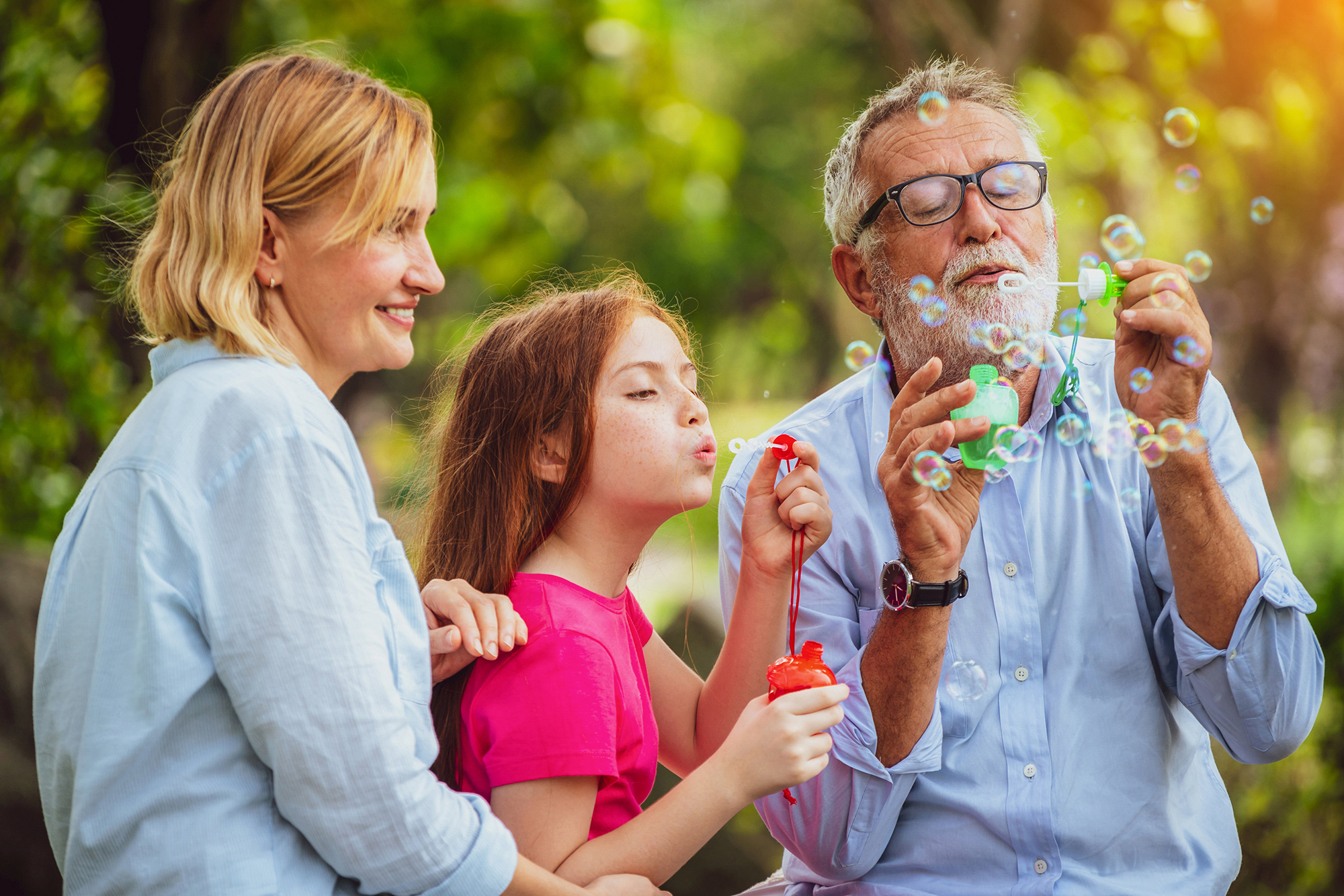 A family of three joyfully blows bubbles together outdoors, enjoying a pleasant day.
