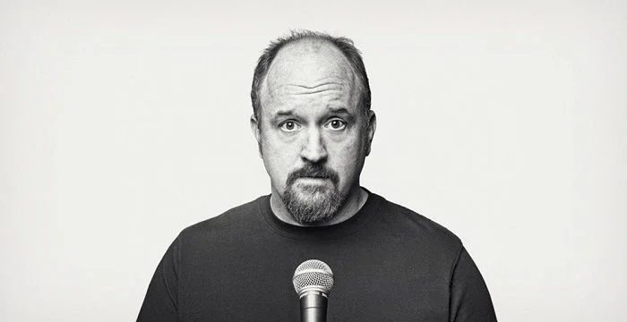 Black and white portrait of Louis C.K. with a microphone