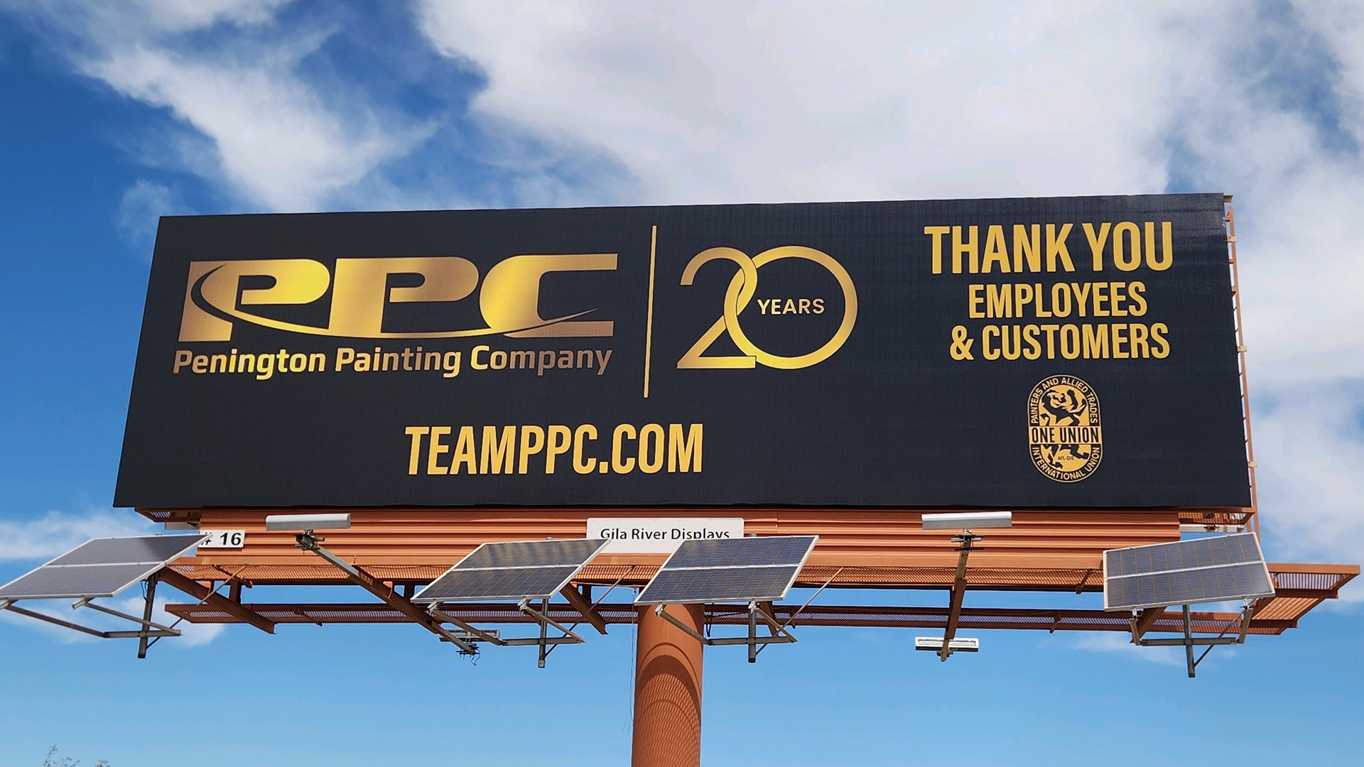 Billboard with "Penington Painting Company" logo and "20 Years" in gold. Text thanks employees and customers. Bright blue sky background.