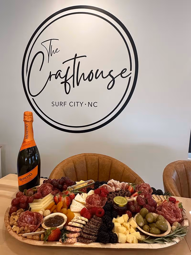 A bottle of wine sits on a table with a cheese platter and a sign that says "The Crafthouse".