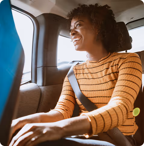 A woman in a striped shirt smiles while sitting in the backseat of a car.