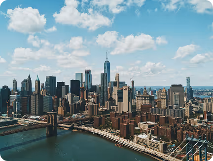 City skyline with numerous skyscrapers under a blue sky, with a bridge spanning the river below.