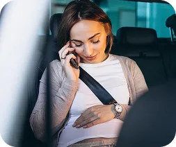 A woman in a car talks on her phone, wearing a seatbelt.
