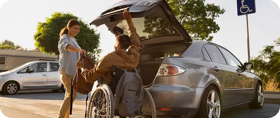A person in a wheelchair loads a bag into a car's open trunk.