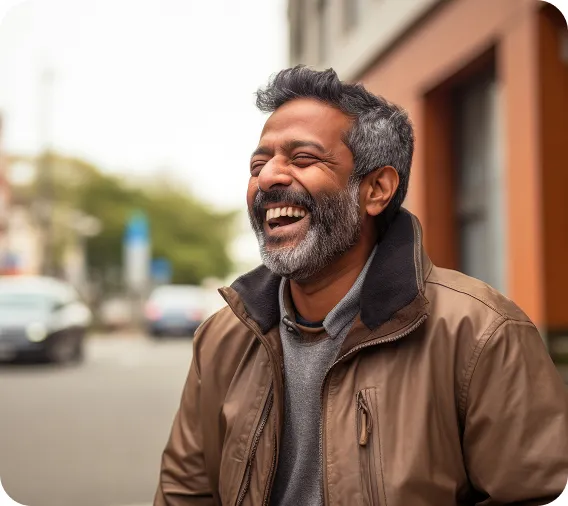 A man with a beard is laughing joyfully on a city street.