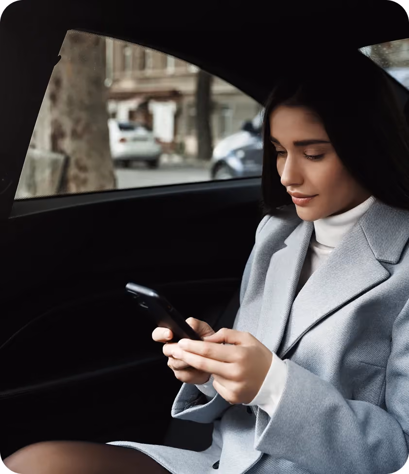 Elegant woman in a gray suit sitting in the back seat of a car, focused on her phone.