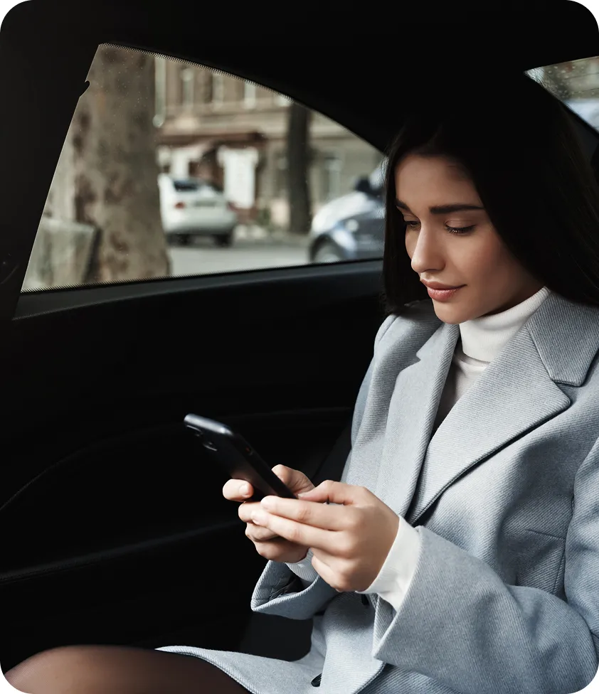 Elegant woman in a gray suit sitting in the back seat of a car, focused on her phone.