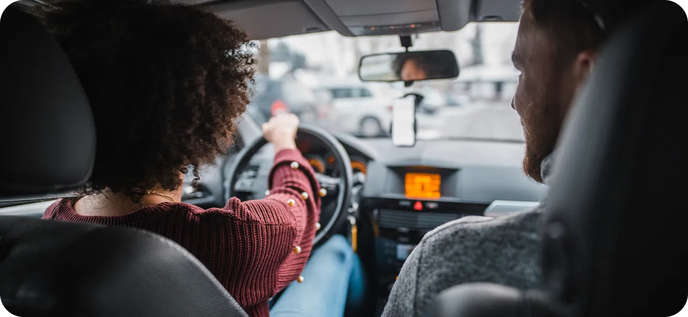 Two people in a car; one is driving, and the other is sitting in the passenger seat.